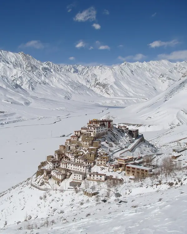 Whitewashed monastery buildings stacked on a snowy hill, with mountains behind